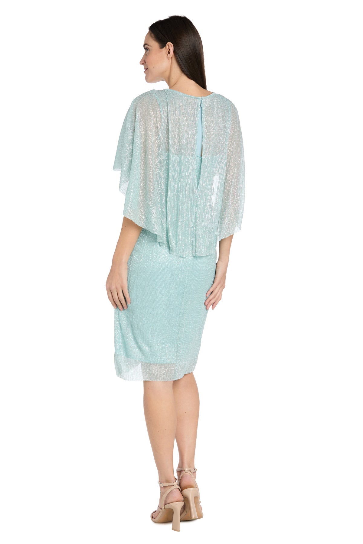 A woman stands facing away, wearing the R&M Richards 3195P Caped Knee-Length Party Dress with loose, semi-sheer sleeves and beige heeled sandals.